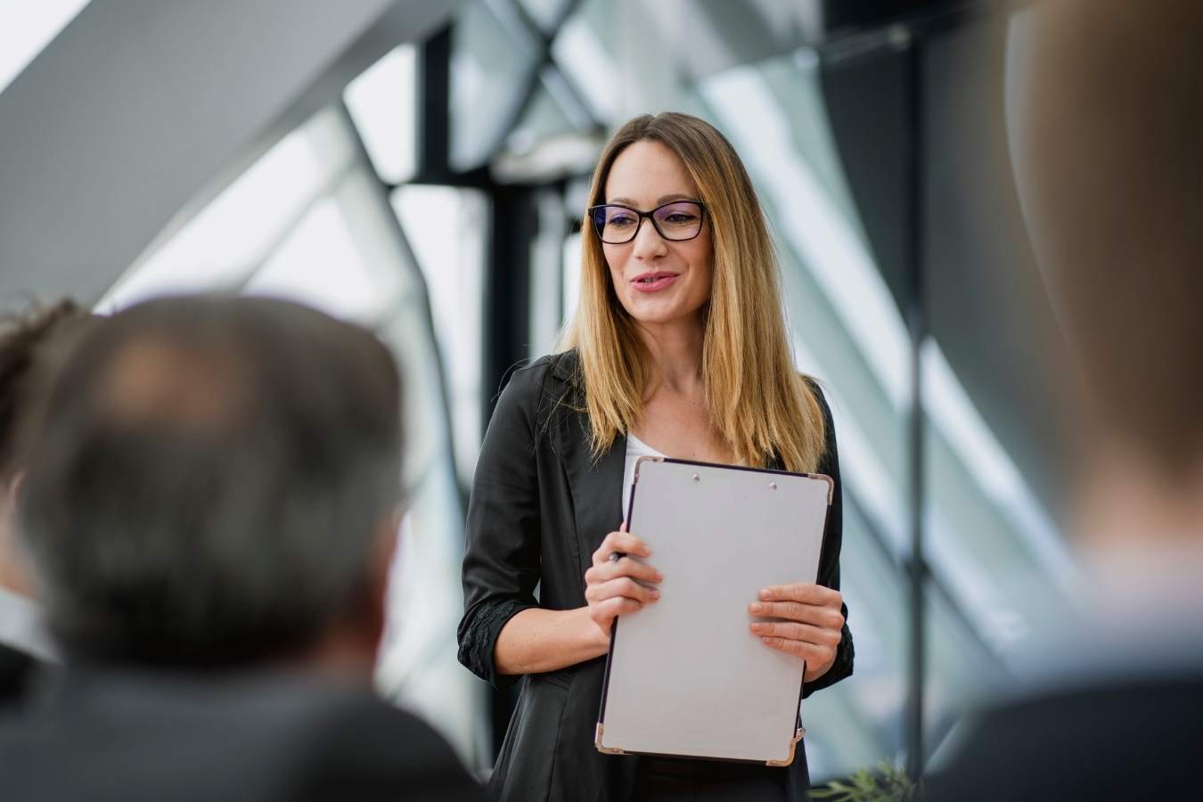 Female entrepreneur in glasses pitching idea at team meeting holding clipboard.jpg