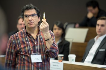 A professor holding up a pen, speaking to the class