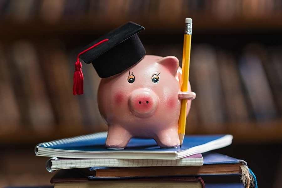 Piggy bank with graduation cap on books holding a pencil