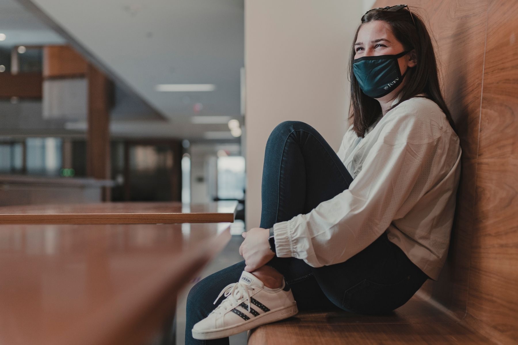 Ivey student sitting on wood bench wearing a green ivey face mask