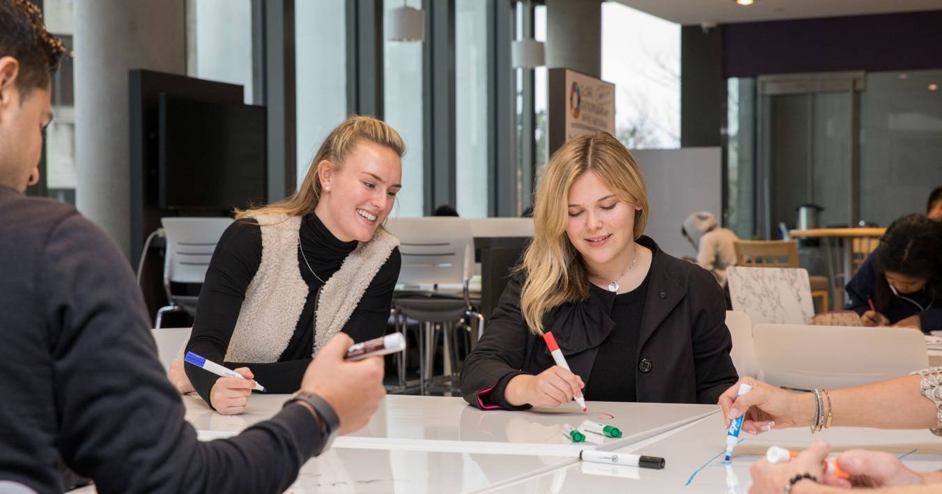 Two Female Entreprnuers Writing On Whiteboard Tables In Coworking Space